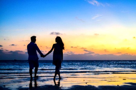 Man And Woman Holding Hands Walking On Seashore During Sunrise