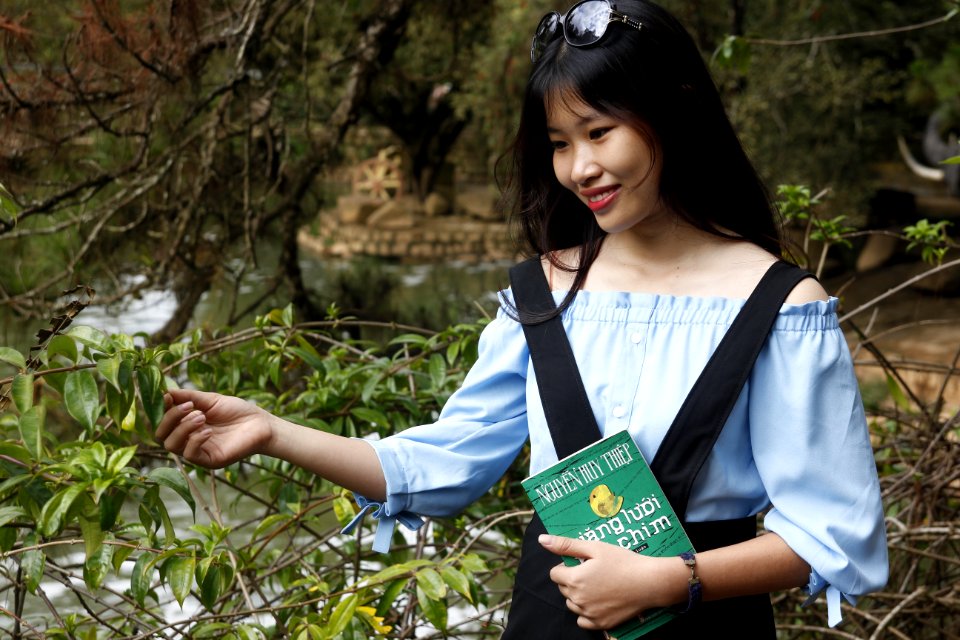 Woman Wearing Blue Off-shoulder Blouse Holding Book Next To Green Leaf Plant photo