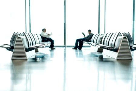 Two Men Sitting In Front Of Each Other On White Gang Chairs In Airport Waiting Area photo