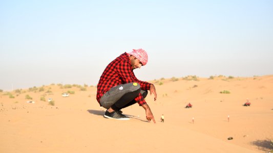 Man In Flannel Shirt Sitting On Sand photo