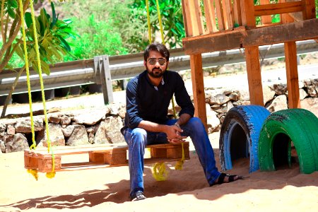 Man Wearing Black Dress Shirt And Blue Jeans Sitting On Wooden Pallet Swing photo