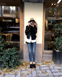 Woman Wearing Black Jacket And Blue Jeans Leaning On Wall photo