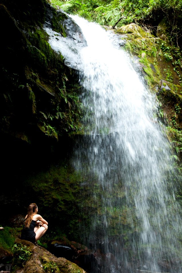 Photo Of Woman Sitting On Rock Facing The Waterfalls