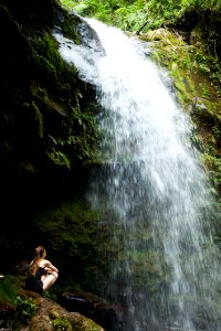 Photo Of Woman Sitting On Rock Facing The Waterfalls