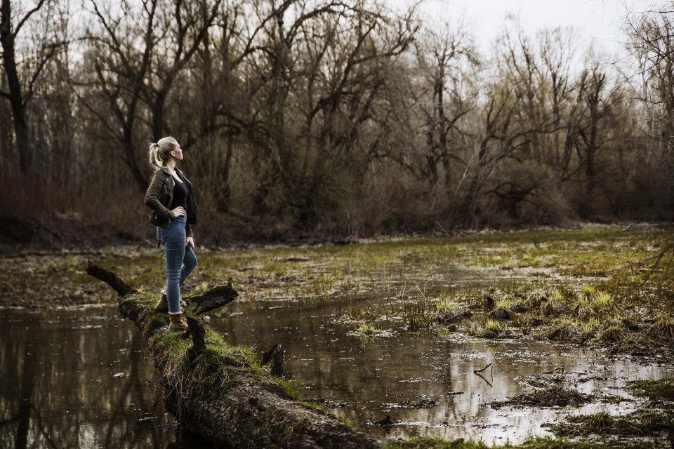 Woman Standing On Driftwood Above Body Of Water