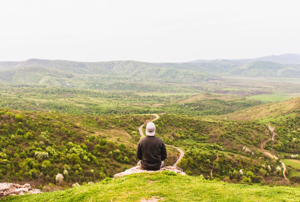 Man Sitting On Mountain Facing Forest Field