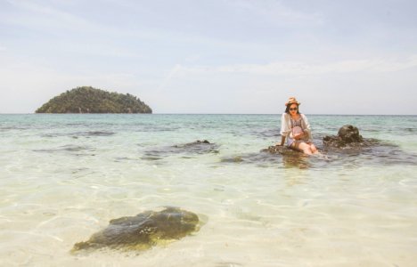 Woman Wearing White Top Sitting On Brown Rock On Body Of Water During photo