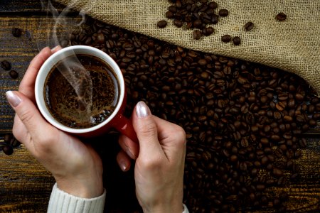 Person Holding Red Cup Of Coffee Cup With Coffee Above Coffee Beans photo
