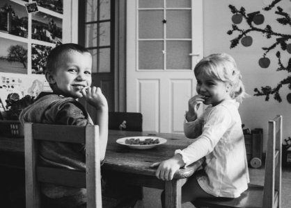 Grayscale Photo Of Two Kids Sitting On Dining Table Chairs photo