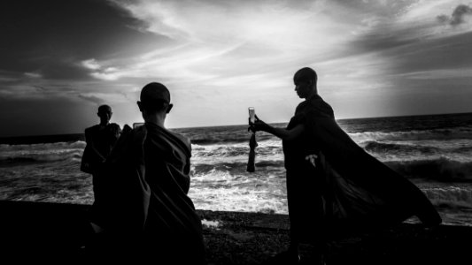 Greyscale Photography Of Three Monks Near Ocean photo