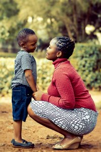 Tilt Shift Lens Photography Of Woman Wearing Red Sweater And White Skirt While Holding A Boy Wearing White And Black Crew-neck Shi