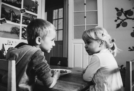 Grayscale Photo Of Boy And Girl Sitting On A Dining Table Chairs photo