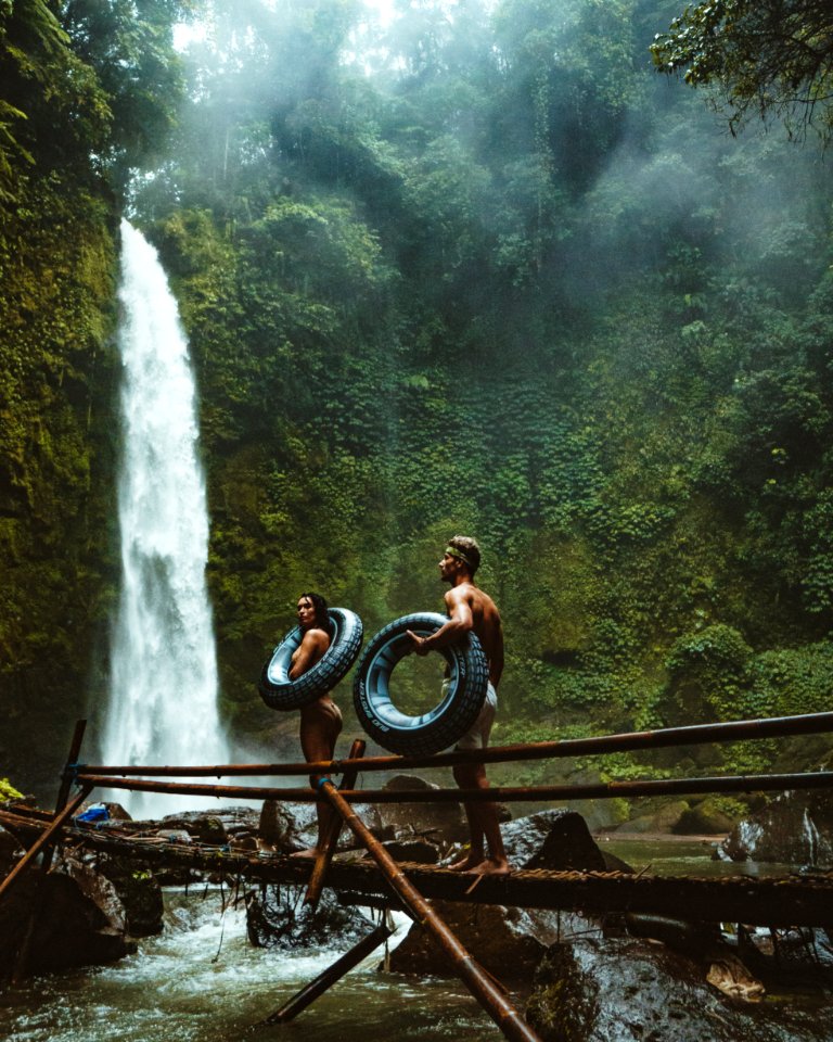 Two Person Carrying Black Inflatable Pool Float On Brown Wooden Bridge Near Waterfalls photo