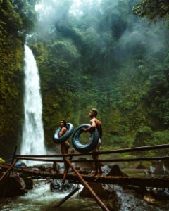 Two Person Carrying Black Inflatable Pool Float On Brown Wooden Bridge Near Waterfalls photo