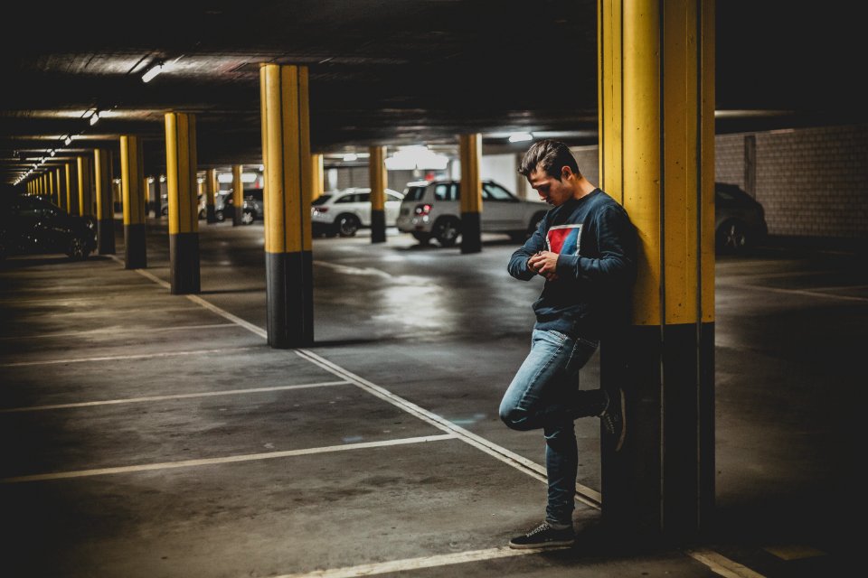 Man In Dark-gray Crew-neck Sweater Standing Leaning To Post In Parking Lot