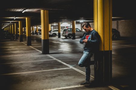 Man In Dark-gray Crew-neck Sweater Standing Leaning To Post In Parking Lot photo