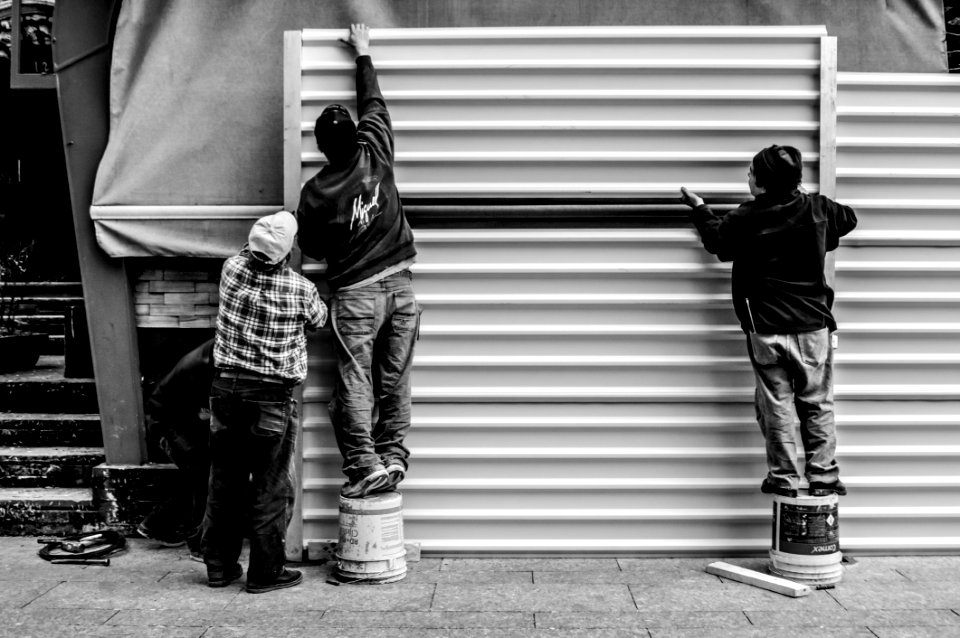Grayscale Photo Of Three Men Arranging Metal Wall