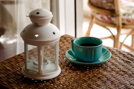 White Candle Lantern Beside Of Blue Ceramic Coffee Mug On Wicker Table photo
