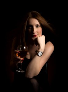 Woman Wearing Black Dress Holding Clear Wine Glass In Dark Room photo
