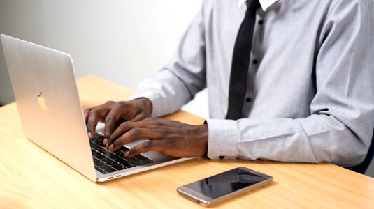Person Sitting In Front Of Table Using Laptop Beside Smartphone
