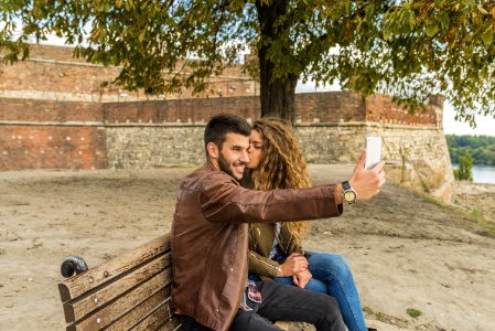 Woman And Man Sitting On Brown Wooden Bench Kissing photo