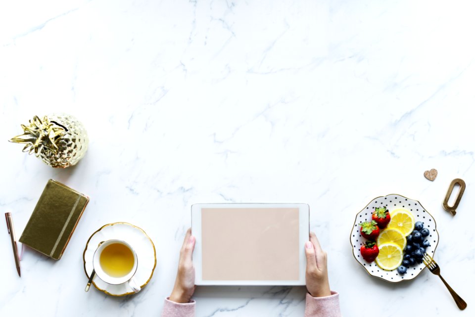 Person Holding White Tablet Computer Beside Teacup And Saucer Of Blueberries