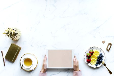 Person Holding White Tablet Computer Beside Teacup And Saucer Of Blueberries