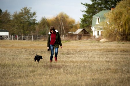 Woman Wearing Brown Zip-up Jacket And Blue Denim Jeans Walking Beside Short-coated Black Dog At Daytime photo