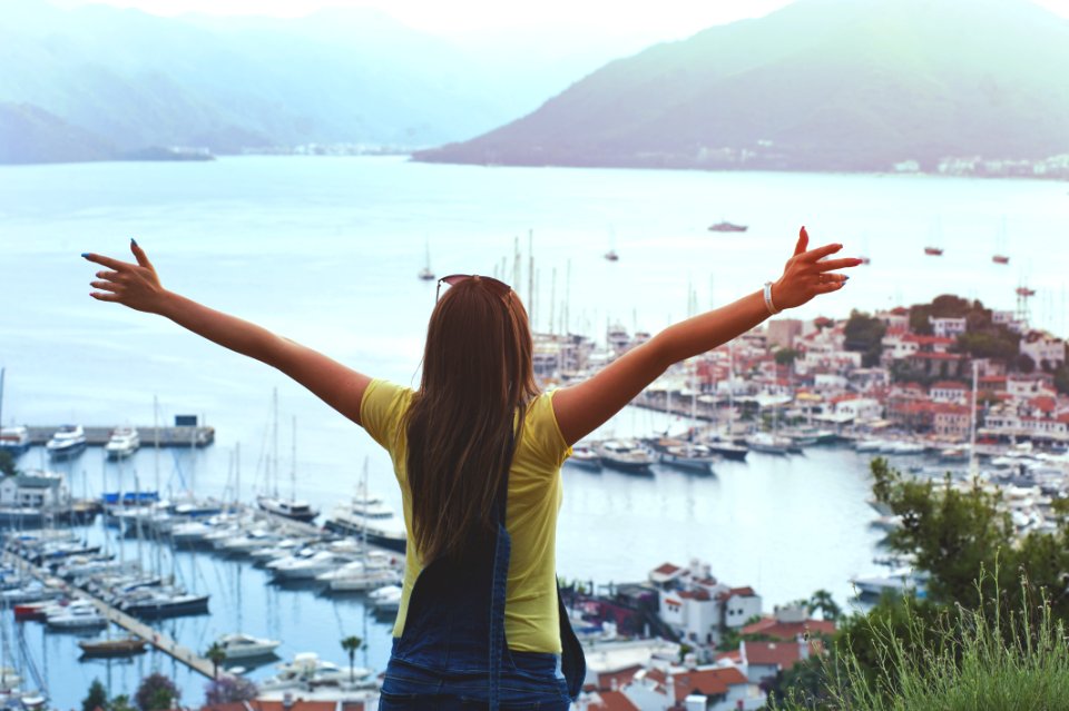 Woman Raising Her Hands Facing Cityscape Near Body Of Water