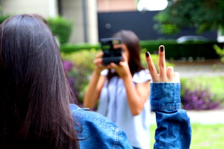 Woman Holding Camera While Taking Picture Of A Woman With A Peace Finger Sign