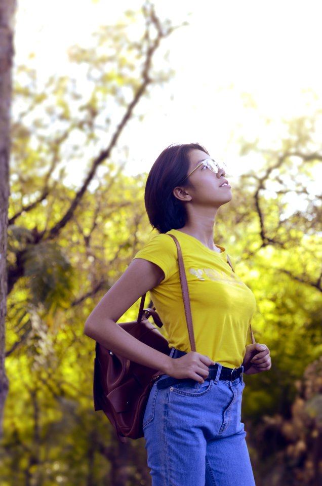Woman Wearing Yellow Shirt And Looking Up Surrounded By Trees