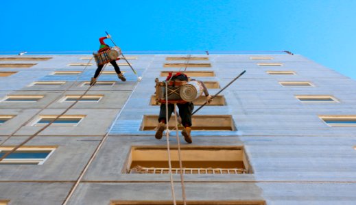 Two People Wearing Harnesses And Painting Building