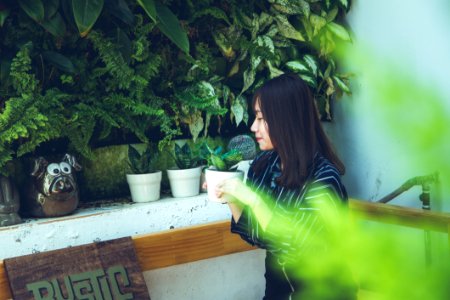 Woman Holding White Clay Pot With Green Plant Sitting Near White Painted Wall