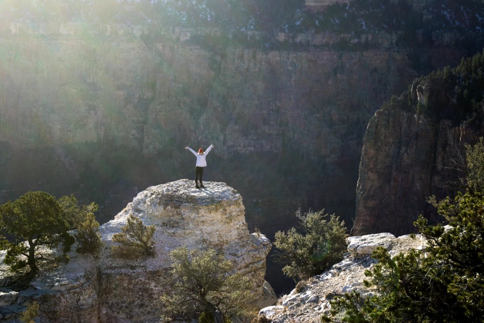 Woman In White Coat And Black Pants Standing On Brown Rock Formation Mountain photo