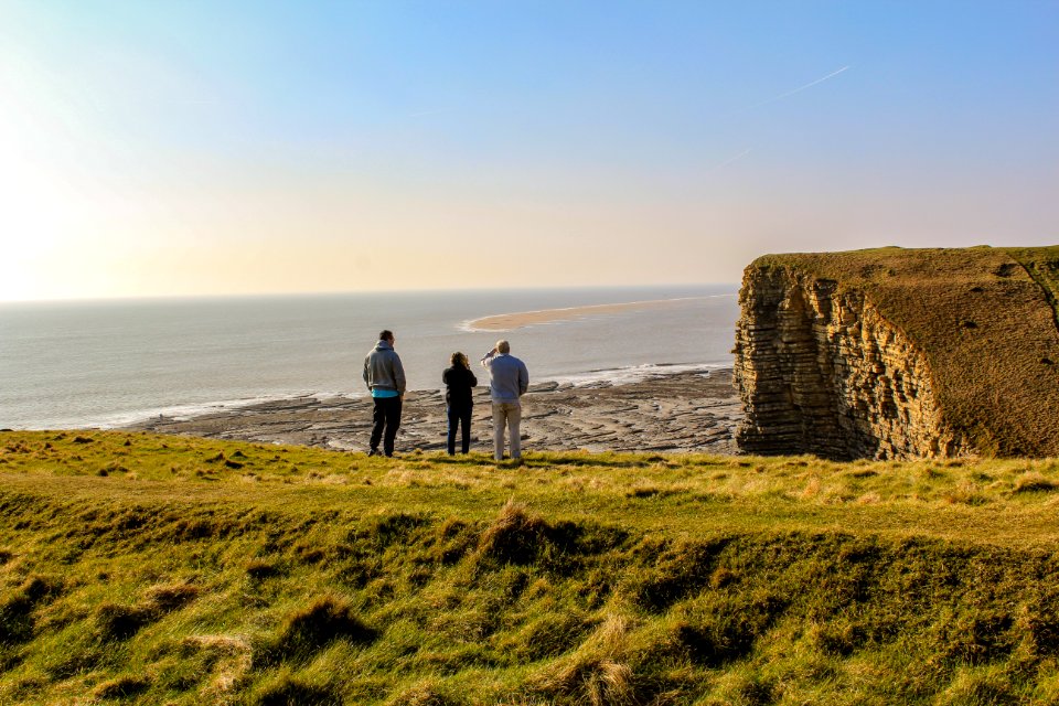 Three People On Top Of Hill Near Body Of Water
