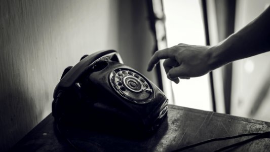 Grayscale Photo Of Rotary Telephone Beside Person Hand photo