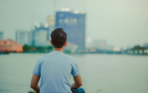 Photo Of Man Wearing Blue Shirt Sitting Looking On High-rise Buildings photo