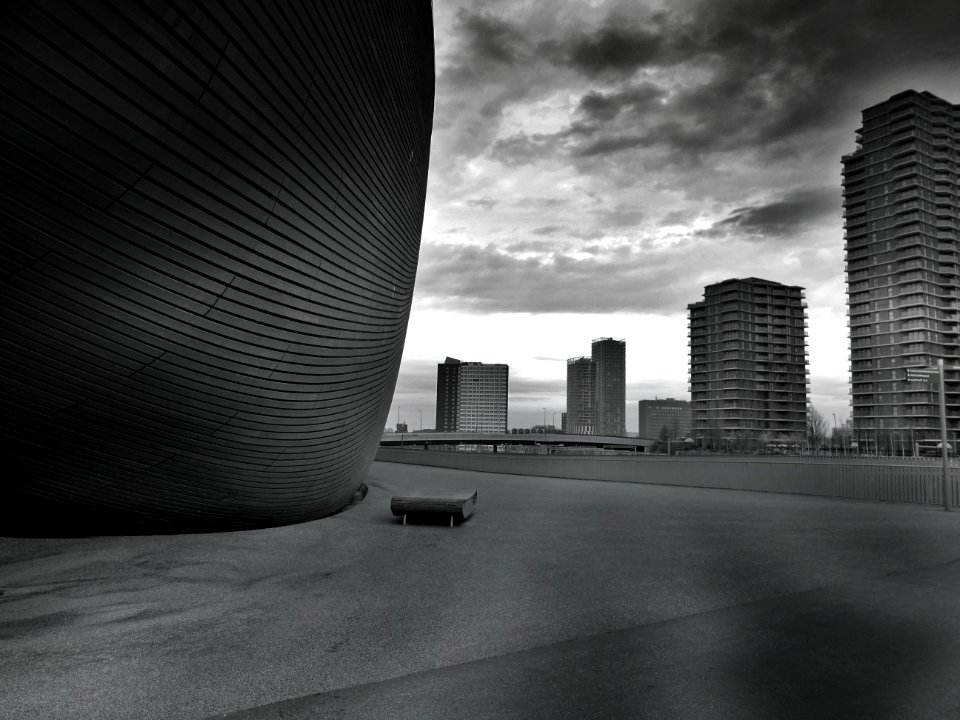 Greyscale Photo Of Bench Beside Tall Building photo