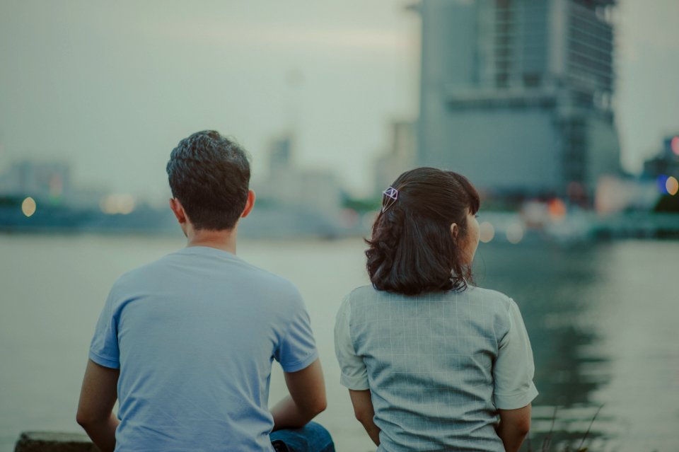 Selective Focus Photography Of Man And Woman Watching Body Of Water And Concrete Buildings