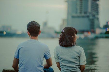 Selective Focus Photography Of Man And Woman Watching Body Of Water And Concrete Buildings photo