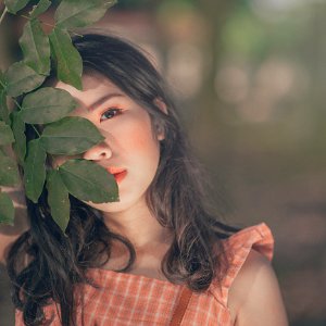 Selective Focus Photography Of Woman In Orange Sleeveless Top Hiding Face Behind Trees Leaf photo