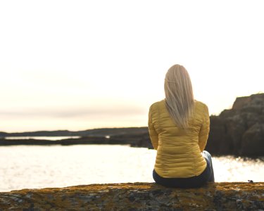Woman Wearing Yellow Bubble Jacket Sitting In Front Of Sea photo