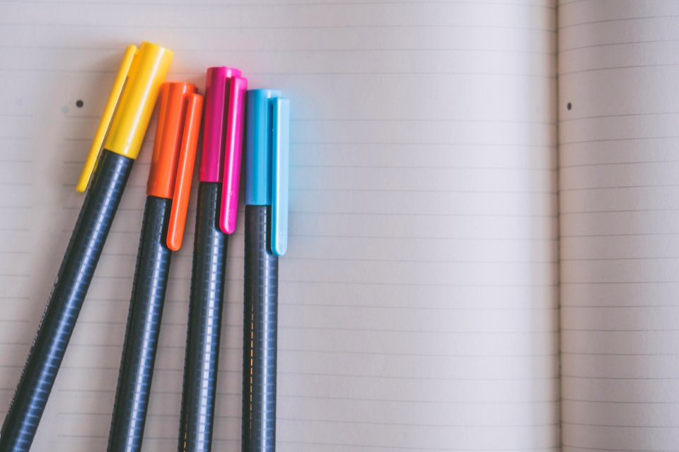 Yellow Orange Pink And Blue Coloring Pens On White Notebook