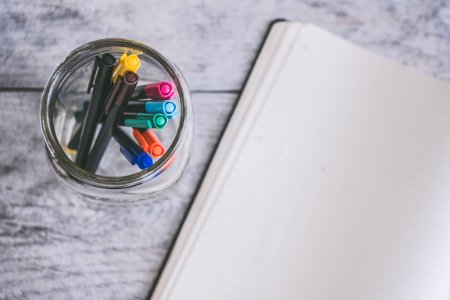 Clear Glass Jar Filled Of Coloring Pens Beside Of White Sketch Pad