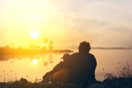 Two People On Grass Beside Body Of Water During Golden Hour