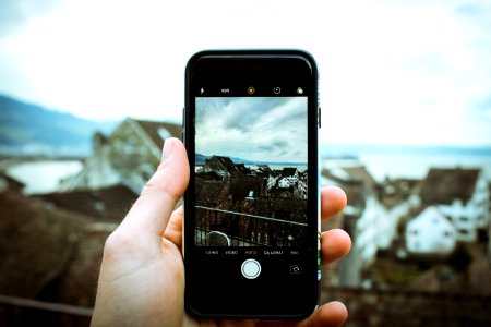 Person Holding Black Smartphone Taking A Picture Of Brown House At Daytime photo