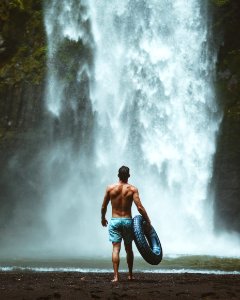 Man Wearing Blue Shorts Holding Vehicle Tire Facing Waterfalls photo