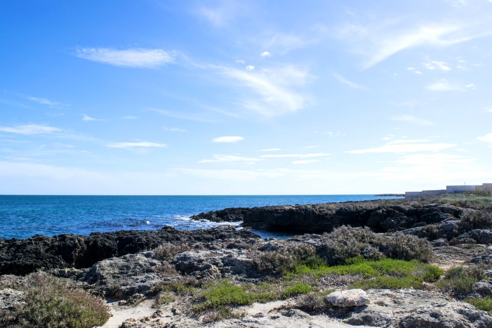 Wavy Sea Beside Rock Formations Near Sea Shore With Grasses Under Blue Cloudy Sky At Daytime photo