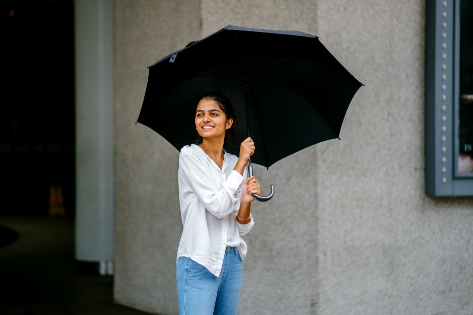 Photo Of Woman Wearing White Long-sleeved Shirt And Blue Jeans Holding Black Umbrella