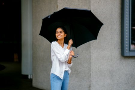 Photo Of Woman Wearing White Long-sleeved Shirt And Blue Jeans Holding Black Umbrella photo